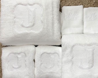 May include: Set of six white towels with embroidered letter J in a decorative frame. The towels are arranged in a row, with the largest towel in the center and two smaller towels on either side. The towels are all made of a soft, absorbent material.