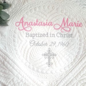 May include: White quilted baby blanket with pink embroidery that reads "Anastasia Marie Baptized in Christ October 29, 1960". A silver cross is embroidered in the center.