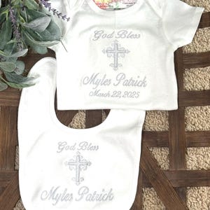 Puede incluir: Babero y body de beb&eacute; blancos con bordado plateado. El bordado dice "God Bless Myles Patrick March 22, 2025".