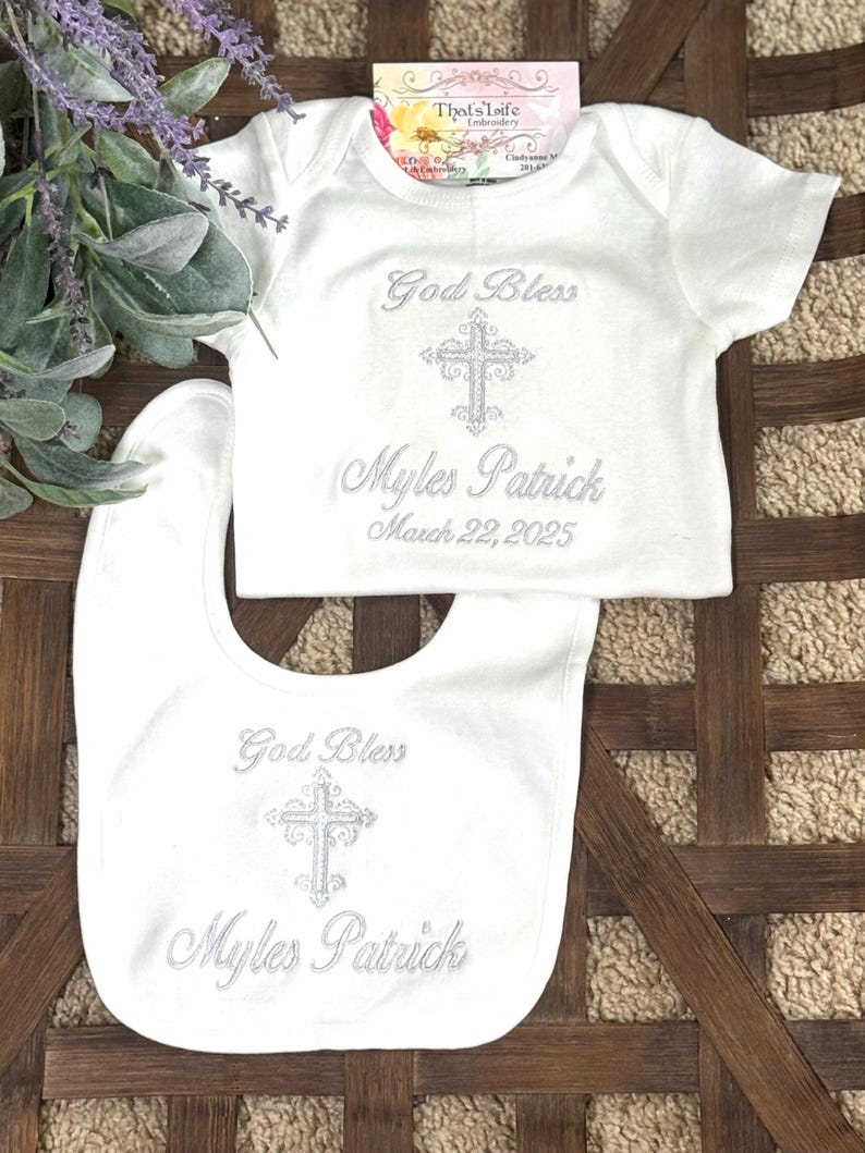 Puede incluir: Babero y body de beb&eacute; blancos con bordado plateado. El bordado dice "God Bless Myles Patrick March 22, 2025".