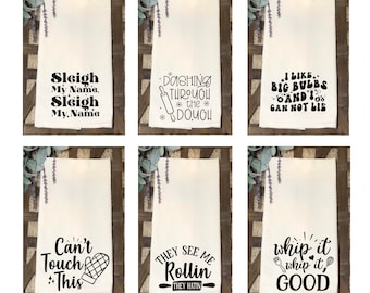 May include: Six white kitchen towels with black text and graphics. The towels feature various holiday-themed phrases, including "Sleigh My Name", "Dashing Through the Dough", "I Like Big Bulbs and I Can Not Lie", "Can't Touch This", "They See Me Rollin' They Hatin'", and "Whip It Whip It Good".