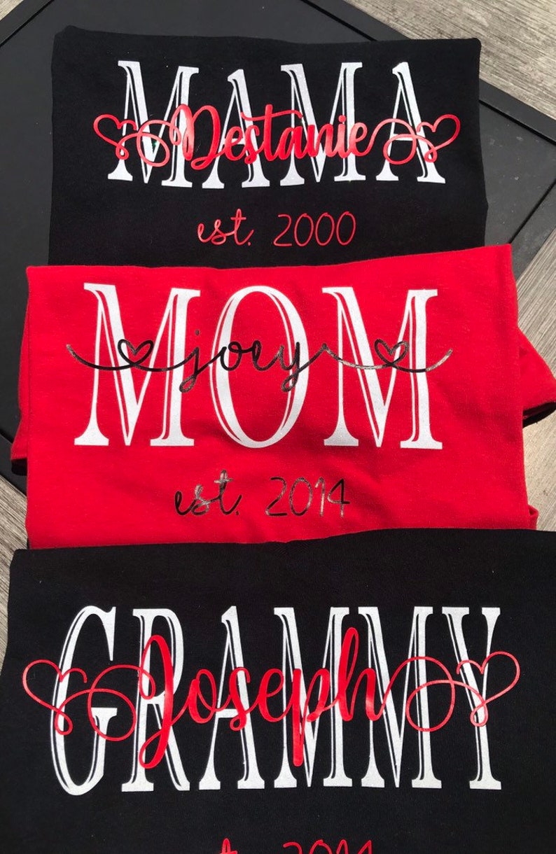 May include: Three black t-shirts with white text and red hearts. The top shirt says "MAMA Destanie est. 2000". The middle shirt says "MOM joey est. 2014". The bottom shirt says "GRAMMY Joseph est. 2014".