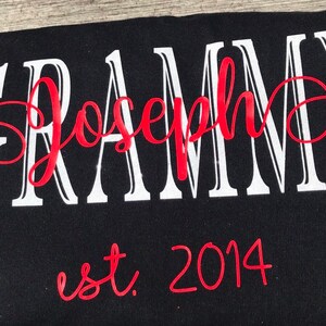 May include: Black t-shirt with white text that reads "GRAMMY Joseph" in a cursive font. The word "Joseph" is in red and the year "2014" is written in red below the text.