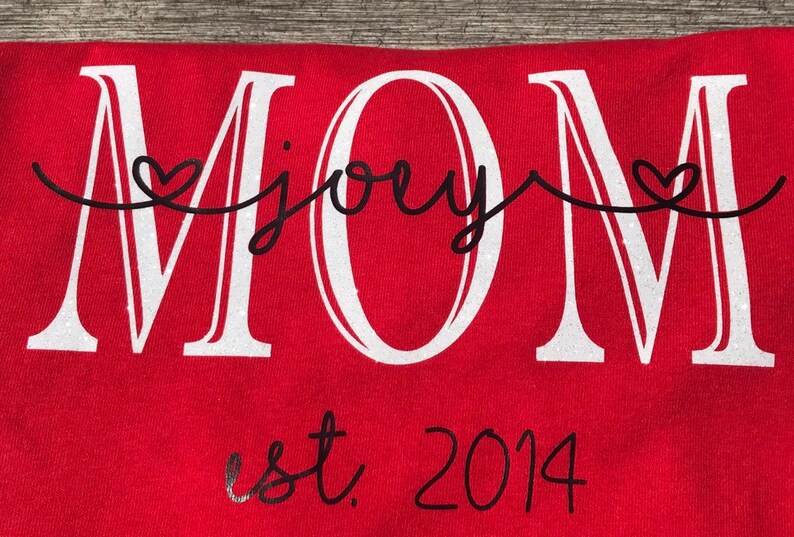 May include: Red t-shirt with white glitter lettering that says "MOM" with the word "joey" written in cursive between the "M"s.  The shirt also has black lettering that says "est. 2014" below the word "MOM".