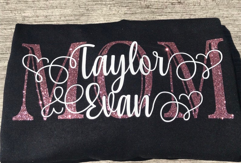 May include: A black t-shirt with a pink glitter MOM design. The names "Taylor & Evan" are written in white cursive lettering.