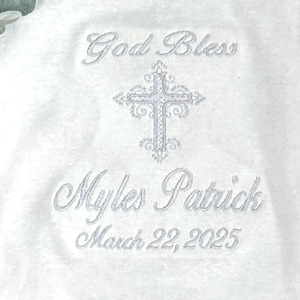 Puede incluir: Unisie blanco para beb&eacute; con bordado plateado. El bordado dice "God Bless Myles Patrick March 22, 2025" e incluye una cruz.