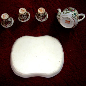 May include: A white porcelain tea set with floral designs. The set includes a teapot, four cups, and a tray.