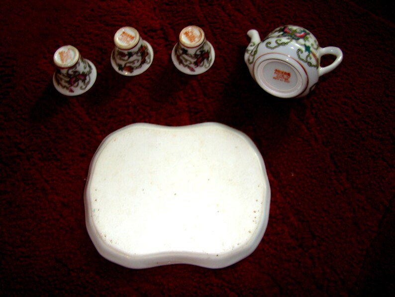 May include: A white porcelain tea set with floral designs. The set includes a teapot, four cups, and a tray.