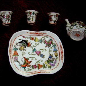 May include: A white porcelain tea set with floral designs. The set includes a teapot, four cups, and a tray.