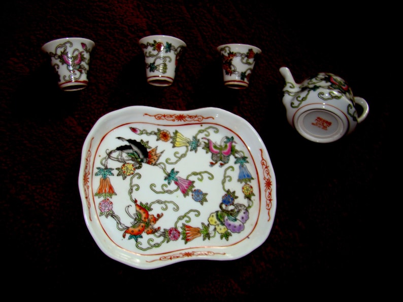 May include: A white porcelain tea set with floral designs. The set includes a teapot, four cups, and a tray.