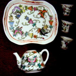 May include: A white porcelain tea set with a floral design. The set includes a teapot, four cups, and a tray. The teapot has a butterfly design on the side. The cups and tray have a floral design with butterflies.