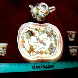 May include: A white porcelain tea set with floral designs. The set includes a teapot, four cups, and a tray. The tray has a scalloped edge and a floral design.