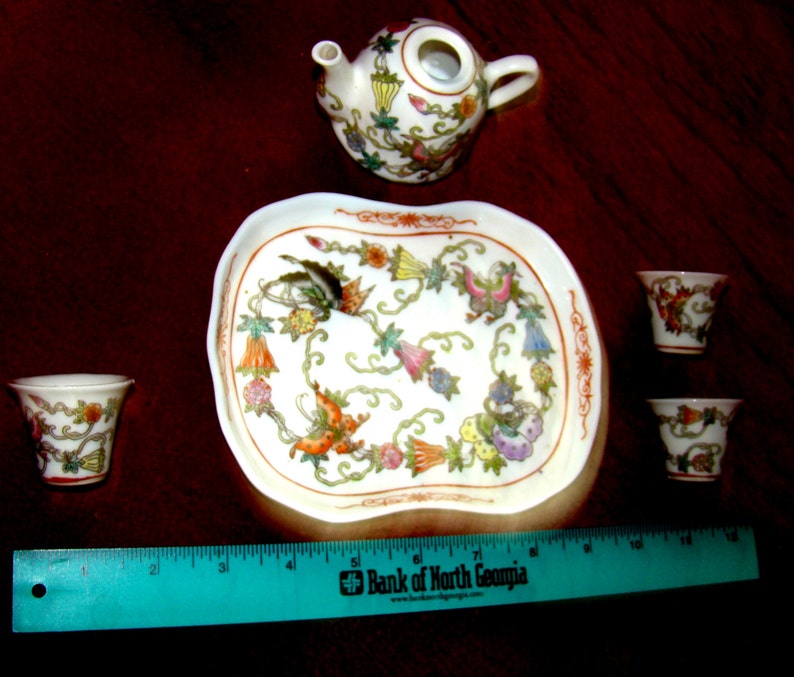 May include: A white porcelain tea set with floral designs. The set includes a teapot, four cups, and a tray. The tray has a scalloped edge and a floral design.