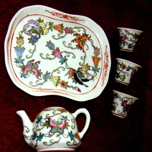 May include: A white porcelain tea set with a floral design. The set includes a teapot, a tray, and four cups. The teapot has a butterfly design on the side. The tray and cups have a floral design with butterflies.