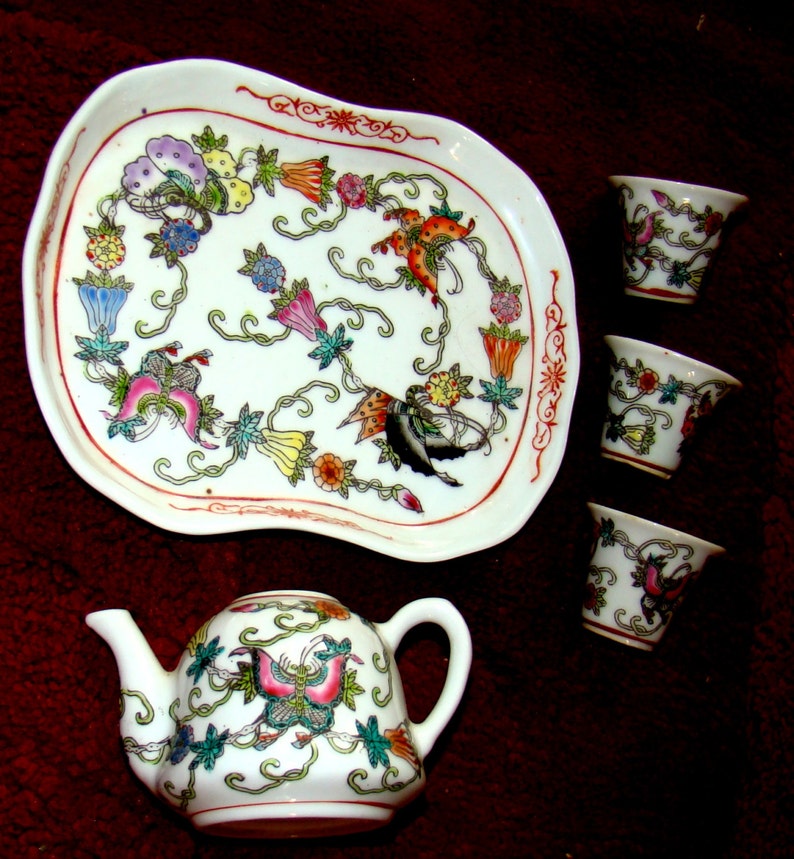May include: A white porcelain tea set with a floral design. The set includes a teapot, a tray, and four cups. The teapot has a butterfly design on the side. The tray and cups have a floral design with butterflies.