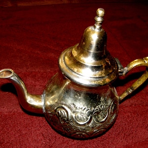 Puede incluir: Una tetera de plata con un diseño ornamentado y una tapa con un pomo. La tetera tiene un pico y una asa.