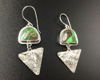 May include: A pair of silver earrings with green and brown gemstone accents. The earrings feature a triangular shape with a textured surface and a curved top with a gemstone.