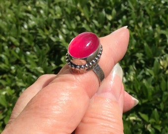 May include: A silver ring with a pink oval gemstone set in a beaded bezel.