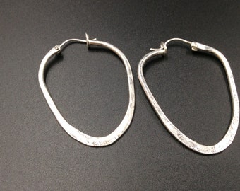 May include: A pair of silver hoop earrings with a hammered texture and an oval shape.