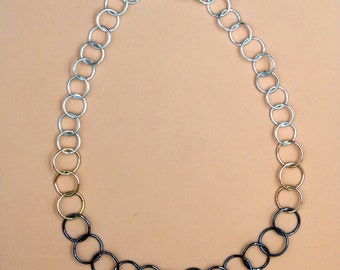 May include: A silver, gold and black chain necklace made of linked circles.