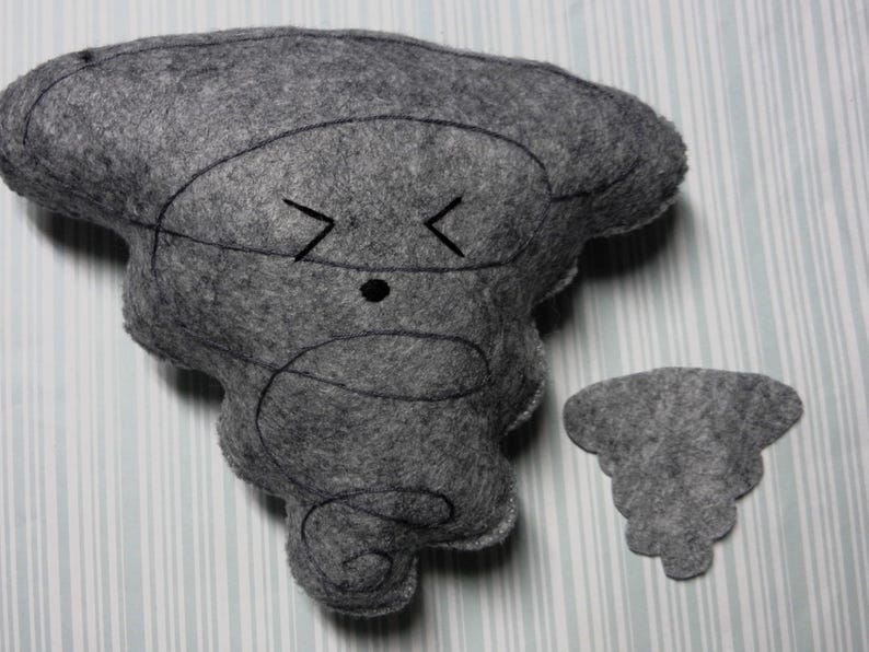 Pu&ograve; includere: Un giocattolo di peluche in feltro grigio a forma di tornado con un viso ricamato nero. Il giocattolo ha una piccola nuvola di feltro grigio attaccata ad esso.