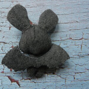 May include: A gray felt bat with large ears and wings. The bat is lying on a blue and white painted wooden surface.