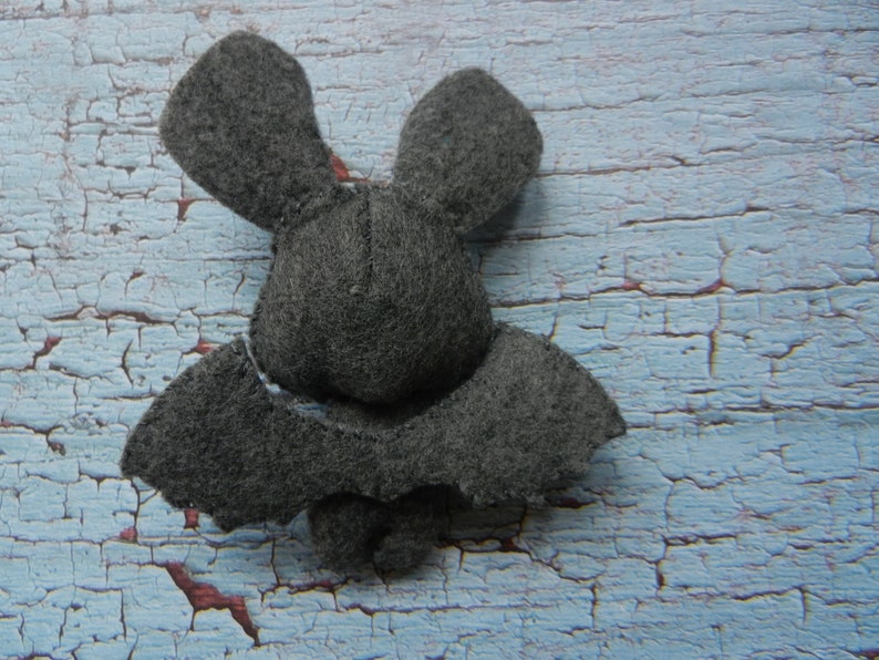 May include: A gray felt bat with large ears and wings. The bat is lying on a blue and white painted wooden surface.