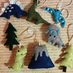 May include: A set of felt ornaments featuring a variety of dinosaurs, a volcano, and a pine tree. The ornaments are all hand-sewn and have a rustic, handmade look.