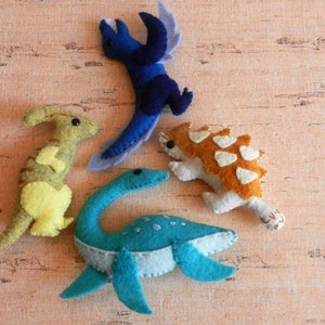 May include: Five felt dinosaur toys, including a blue pterodactyl, a yellow dinosaur, a blue plesiosaur, and a brown ankylosaurus.