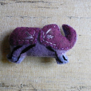 May include: Purple felt elephant toy with embroidered details. The elephant has a small trunk and large ears.