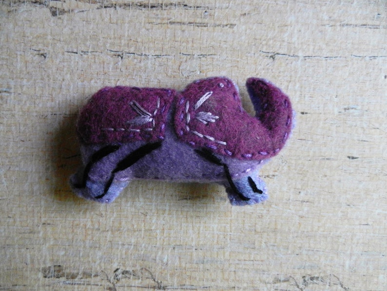 May include: Purple felt elephant toy with embroidered details. The elephant has a small trunk and large ears.