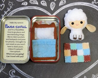 May include: A handmade felt travel set featuring a sheep plushie, a miniature bed in a tin, and a patchwork blanket. The tin contains text that reads "Hello! My name is Baaa-Shful". The set is designed for imaginative play.