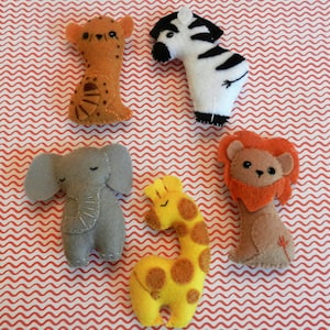 May include: A set of six felt animal toys, including a zebra, lion, giraffe, elephant, and two cats. The toys are all handmade and have a simple, whimsical design.