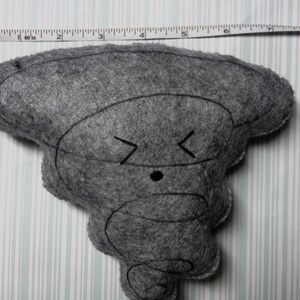 Pu&ograve; includere: Un giocattolo di peluche in feltro grigio a forma di tornado dei cartoni animati con un occhio nero e una smorfia. Il giocattolo &egrave; alto circa 18 cm.