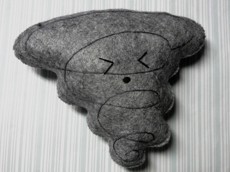 Pu&ograve; includere: Un giocattolo di peluche grigio a forma di tornado con un viso da cartone animato. Il giocattolo ha un occhio nero e una bocca semplice con due linee inclinate.