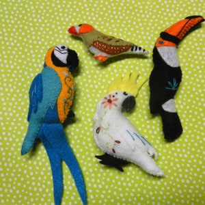 May include: Five felt bird ornaments, including a blue and orange macaw, a white cockatoo, a brown and white finch, and a black and orange toucan.