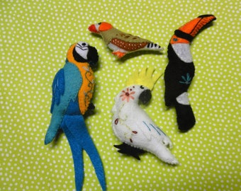 May include: Five felt bird ornaments, including a blue and orange macaw, a white cockatoo, a brown and white finch, and a black and orange toucan.