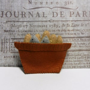 May include: A felt craft of a brown pot with five felt loaves of bread inside. The pot has a white stitched rim and the loaves are beige and gray.