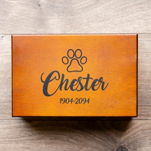 May include: A wooden box with a paw print and the name "Chester" engraved on the top. The dates "1904-2094" are also engraved on the box.