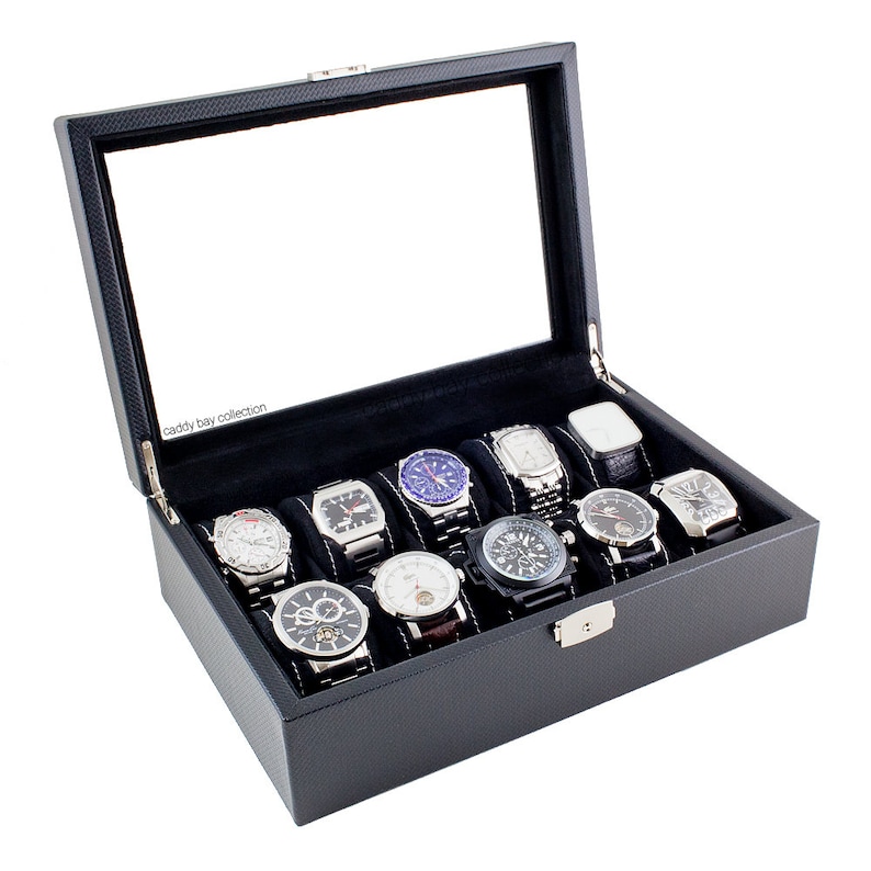 K&ouml;nnte beinhalten: Schwarze Lederuhrenbox mit Glasdeckel und 10 F&auml;chern zur Aufbewahrung von Uhren. Die Box hat ein Karbonfaser-Muster und der Text "caddy bay collection" ist innen aufgedruckt.