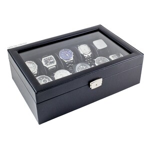 K&ouml;nnte beinhalten: Schwarze Lederuhrenbox mit Glasdeckel und silbernem Schloss. Die Box hat 10 F&auml;cher f&uuml;r Uhren und der Text "caddy bay collection" ist auf der Vorderseite aufgedruckt.