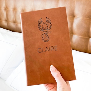 May include: A brown leather journal with a scorpion design and the name "CLAIRE" embossed on the front.