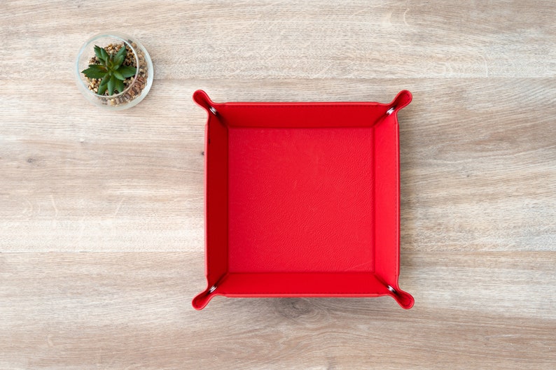 May include: A red leather dice tray with a square shape and a smooth surface. The tray is empty and ready to hold dice.