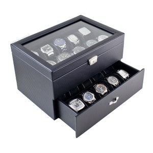 May include: Black leather watch box with a glass top and a drawer. The box has a carbon fiber pattern and a lock. The drawer has 8 slots for watches.