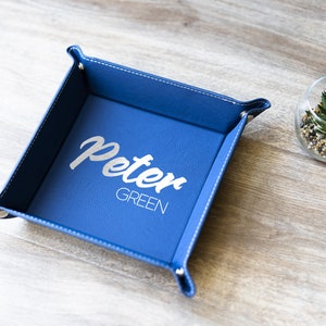 May include: A blue leather catchall tray with white stitching and the name "Peter Green" embossed in silver lettering.