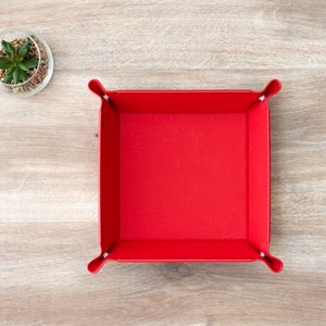 May include: A red leather dice tray with a square shape and a smooth surface. The tray is empty and ready to hold dice.