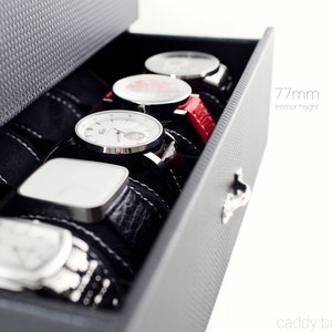 May include: A black watch box with a drawer that is open, revealing five watches with different colored bands. The drawer is labeled "77mm interior height".