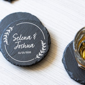 K&ouml;nnte beinhalten: Schwarze Schieferuntersetzer mit einem wei&szlig;en Design mit den Namen "Selena & Joshua" und dem Datum "12/25/2020".