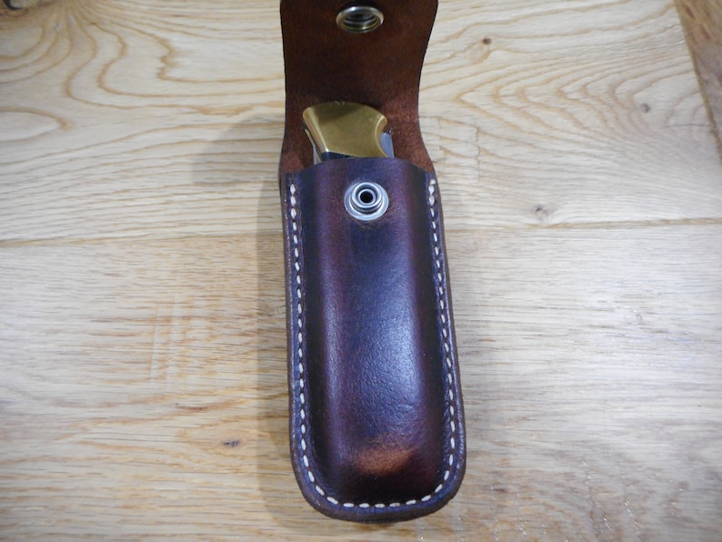 Peut inclure: Un &eacute;tui &agrave; couteau en cuir marron avec des coutures blanches et une fermeture &agrave; pression en laiton.