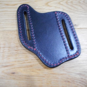 May include: A black leather knife sheath with red stitching. The sheath has two belt loops.